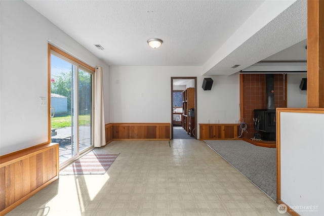 unfurnished dining area with a wood stove, a wainscoted wall, a textured ceiling, tile patterned floors, and wood walls