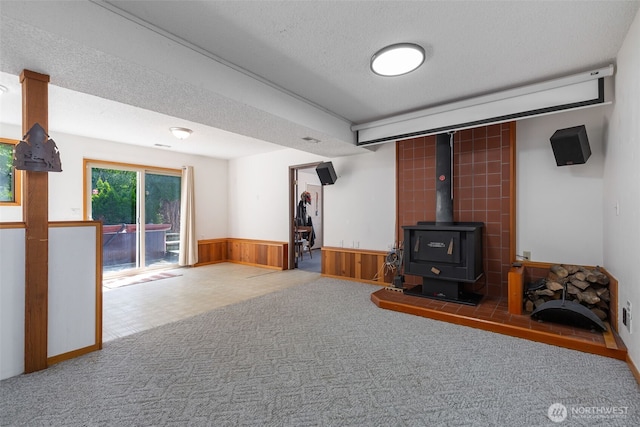 living room featuring wainscoting, a wood stove, a textured ceiling, carpet flooring, and wood walls