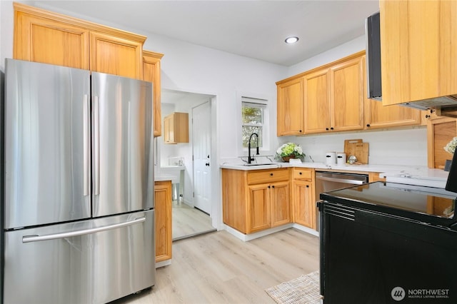 kitchen with freestanding refrigerator, a sink, light countertops, light wood-style flooring, and recessed lighting