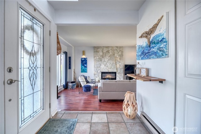 foyer with a stone fireplace, a baseboard heating unit, and light tile patterned flooring