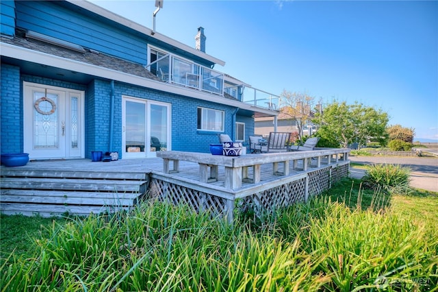 back of property featuring a balcony, brick siding, a wooden deck, and a chimney