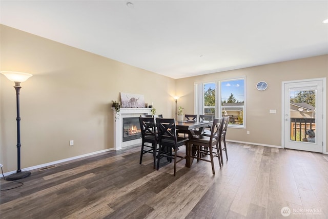 dining room featuring dark wood finished floors, a glass covered fireplace, and baseboards