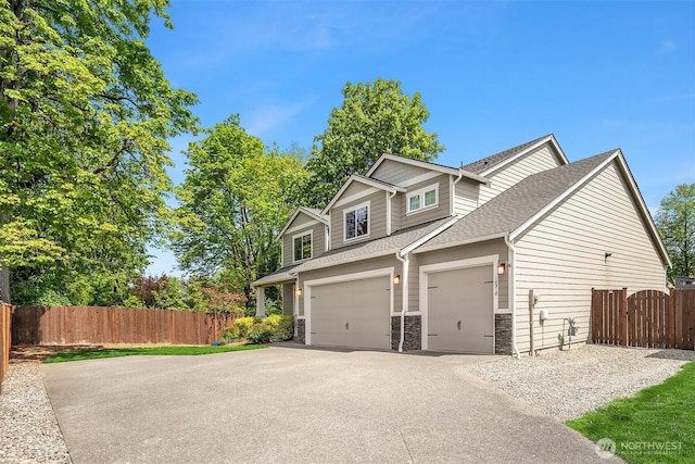 view of side of property with asphalt driveway, fence, roof with shingles, stone siding, and an attached garage
