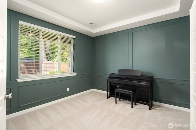 sitting room featuring a decorative wall, light carpet, and a tray ceiling