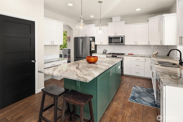 kitchen with appliances with stainless steel finishes, a sink, white cabinets, a center island, and dark wood-style floors