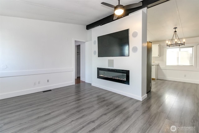 unfurnished living room with a chandelier, wood finished floors, ceiling fan, a glass covered fireplace, and baseboards