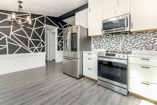 kitchen featuring appliances with stainless steel finishes, light wood-type flooring, tasteful backsplash, white cabinetry, and a chandelier