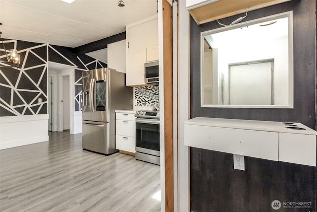 kitchen with appliances with stainless steel finishes, white cabinets, light wood-type flooring, backsplash, and light countertops