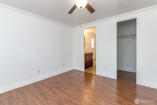 unfurnished bedroom with ornamental molding, wood finished floors, a spacious closet, baseboards, and a closet