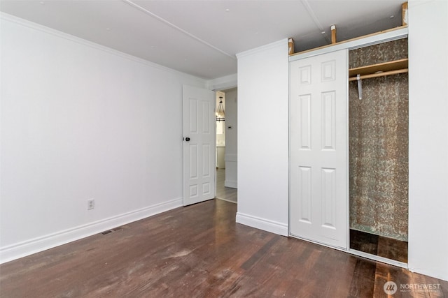 unfurnished bedroom with wood finished floors, crown molding, a closet, and baseboards