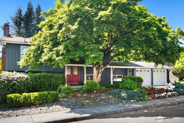 12555 SE 72nd St, Newcastle, WA 98056 - view of property hidden behind natural elements featuring board and batten siding, a garage, and a chimney