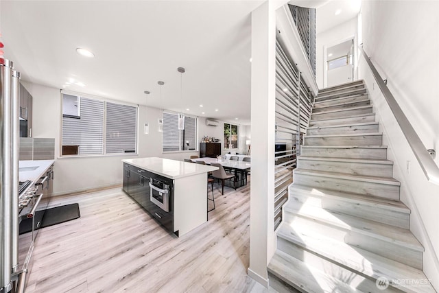 kitchen with light wood-style flooring, stainless steel appliances, a wall unit AC, recessed lighting, and light countertops