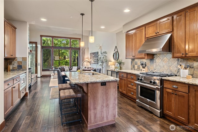 221 Cake Box Ln, Cle Elum, WA 98922 - kitchen with under cabinet range hood, high end range, brown cabinetry, light stone counters, and backsplash