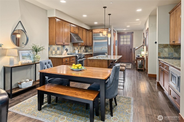 221 Cake Box Ln, Cle Elum, WA 98922 - kitchen with under cabinet range hood, stainless steel appliances, a center island with sink, brown cabinets, and recessed lighting