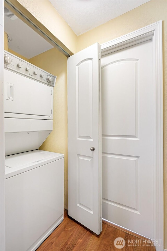 laundry room with stacked washer / dryer and wood finished floors