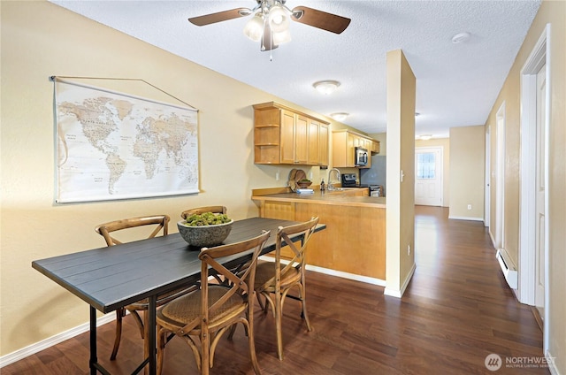 dining area with dark wood-style flooring, a ceiling fan, baseboards, and a textured ceiling