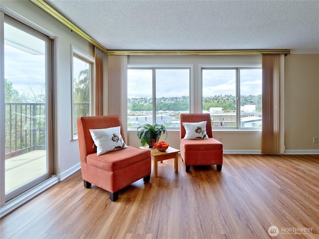 living area featuring crown molding, a textured ceiling, light wood-style floors, healthy amount of natural light, and baseboards