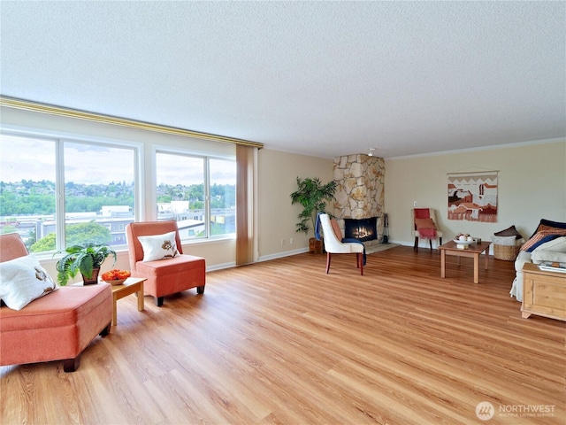 living area featuring a textured ceiling, a stone fireplace, light wood-style flooring, ornamental molding, and baseboards