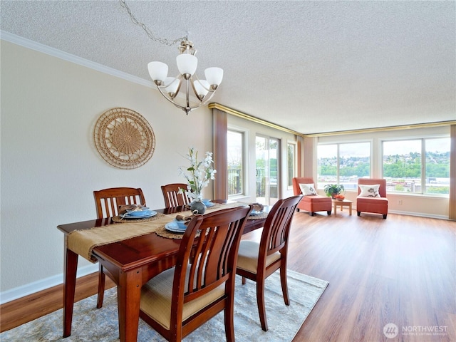 dining space with a chandelier, crown molding, wood finished floors, a textured ceiling, and baseboards
