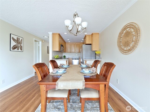dining area with light wood-style floors, baseboards, a chandelier, a textured ceiling, and crown molding