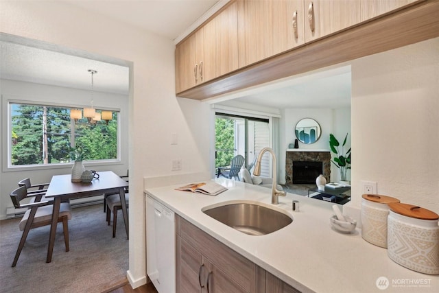 kitchen featuring a sink, light countertops, dishwasher, a stone fireplace, and pendant lighting