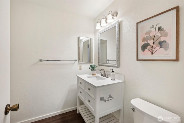 half bath with vanity, toilet, wood finished floors, and baseboards