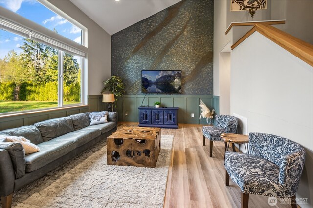 living area featuring wallpapered walls, an accent wall, wood finished floors, a wainscoted wall, and high vaulted ceiling
