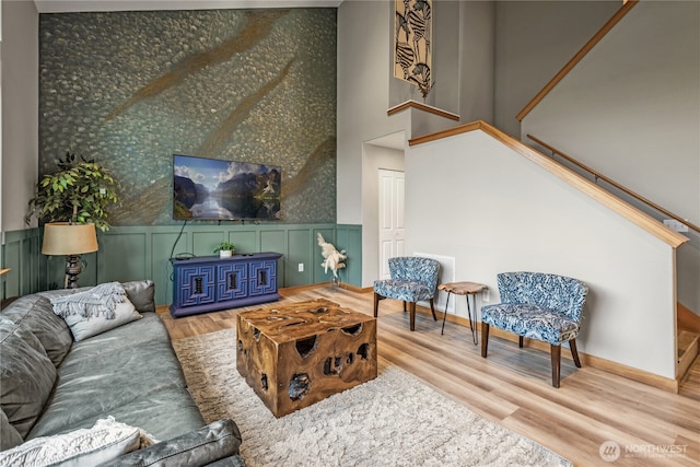 living area with wood finished floors, stairs, wainscoting, baseboards, and a decorative wall