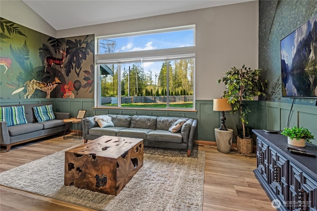 living area featuring wainscoting, wood finished floors, a decorative wall, and lofted ceiling