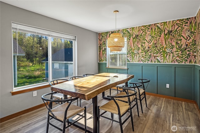 dining room featuring wallpapered walls, wainscoting, wood finished floors, a decorative wall, and baseboards