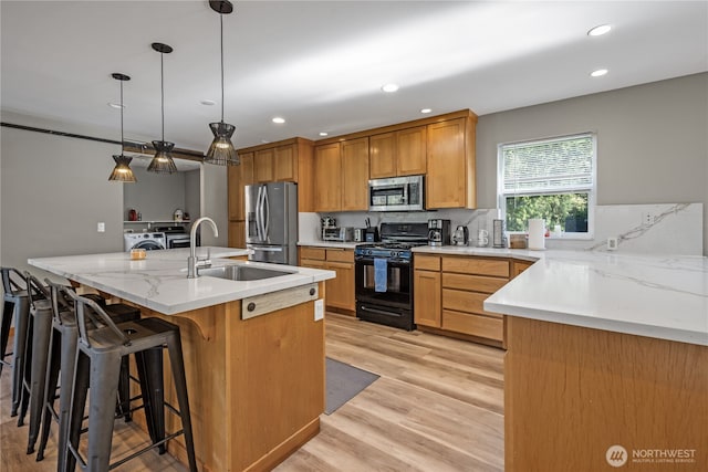 kitchen with stainless steel appliances, washer and clothes dryer, a sink, light wood-style flooring, and recessed lighting