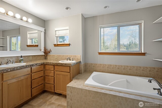 full bath featuring plenty of natural light, tile patterned floors, a garden tub, and double vanity