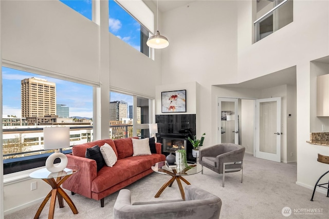 carpeted living area featuring baseboards, a high ceiling, a city view, a tiled fireplace, and french doors