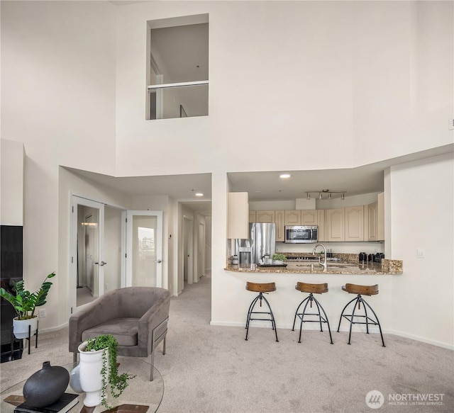 kitchen featuring appliances with stainless steel finishes, light carpet, a breakfast bar area, a towering ceiling, and baseboards