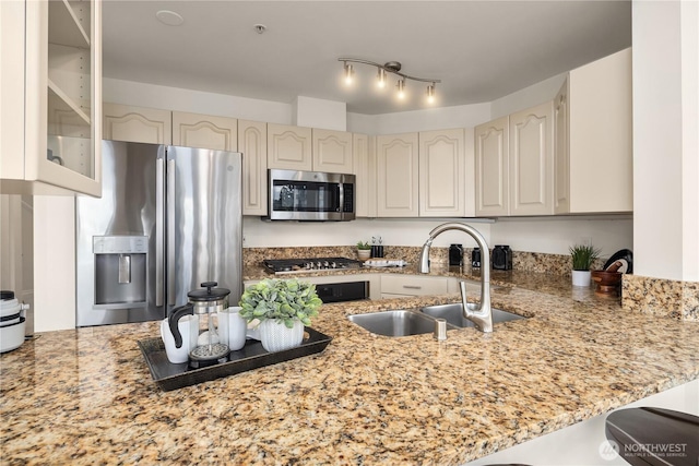 kitchen with stainless steel appliances, a sink, a peninsula, light stone counters, and glass insert cabinets