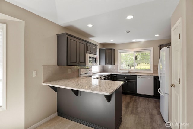 10308 139th Street Ct E, Puyallup, WA 98374 - kitchen with white appliances, a sink, a peninsula, decorative backsplash, and a breakfast bar