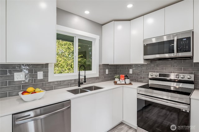 kitchen featuring appliances with stainless steel finishes, a sink, light countertops, white cabinetry, and recessed lighting