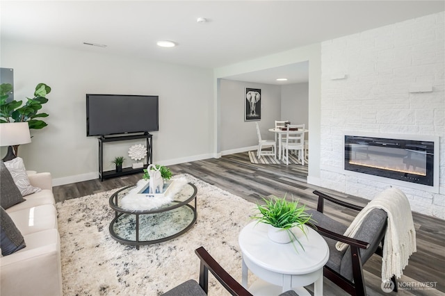 living room with wood finished floors, baseboards, a stone fireplace, and recessed lighting