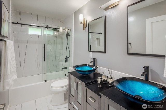 full bath with enclosed tub / shower combo, toilet, and double vanity