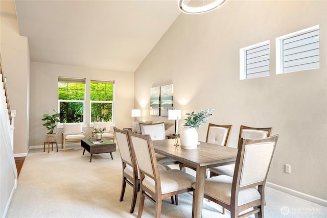 dining area with high vaulted ceiling, light carpet, and baseboards
