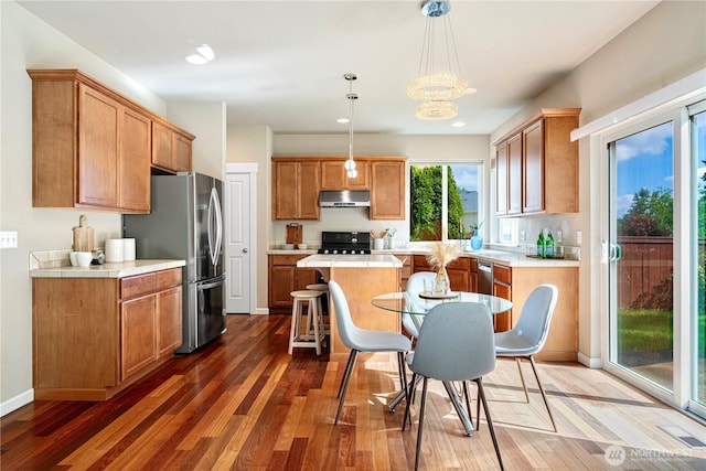 kitchen with under cabinet range hood, light countertops, freestanding refrigerator, wood finished floors, and recessed lighting