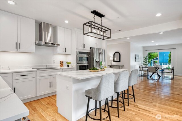 2333 NE 94th St, Seattle, WA 98115 - kitchen featuring wall chimney range hood, stainless steel appliances, light stone countertops, light wood-style flooring, and a kitchen breakfast bar
