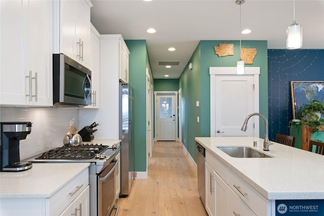 210 E Cedarland Ln, Allyn, WA 98524 - kitchen featuring appliances with stainless steel finishes, a sink, light wood-style flooring, white cabinetry, and an island with sink