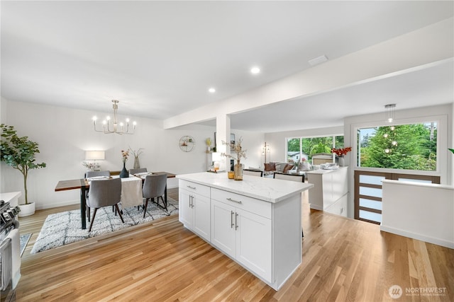 kitchen featuring white cabinetry, light wood finished floors, hanging light fixtures, light stone counters, and a chandelier