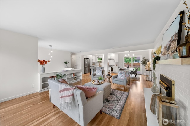 living area with light wood-style flooring, a chandelier, a brick fireplace, and baseboards
