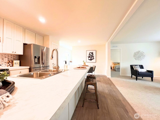 kitchen with stainless steel fridge, white cabinets, a breakfast bar area, wood finished floors, and light countertops