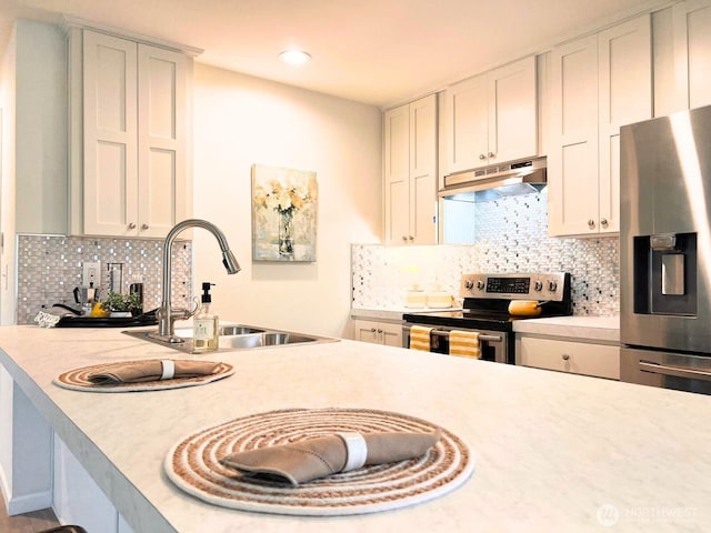 kitchen featuring under cabinet range hood, stainless steel appliances, a sink, light countertops, and decorative backsplash