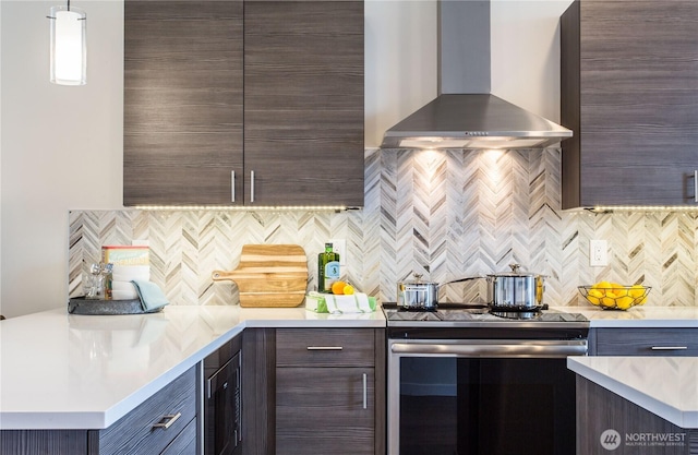 kitchen with wall chimney range hood, stainless steel electric range, tasteful backsplash, light countertops, and dark brown cabinetry