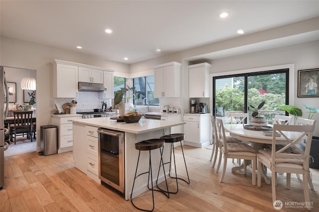 1075 SW 12th St, North Bend, WA 98045 - kitchen featuring beverage cooler, white cabinetry, backsplash, under cabinet range hood, and recessed lighting