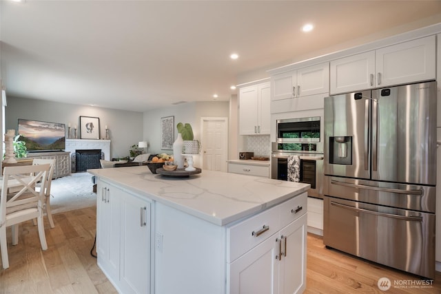 1075 SW 12th St, North Bend, WA 98045 - kitchen with stainless steel appliances, a kitchen island, white cabinets, light wood finished floors, and a fireplace